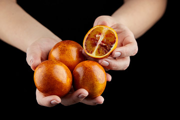 Person holging handful of half and whole red or blood oranges on black background