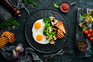 Healthy breakfast. Fried egg with broccoli, mushrooms and bread. On a black stone plate. Top view.