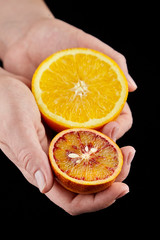 Orange and blood or red orange fruit halves in hands on black background