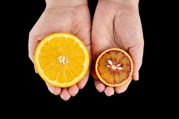 Orange and blood or red orange fruit halves in hands on black background
