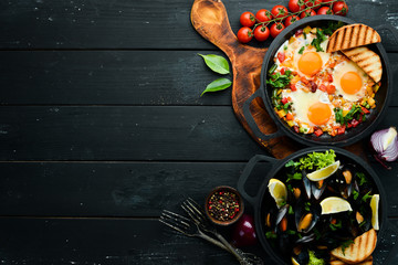Set of dishes in a frying pan on black background. Fried Egg and Mussels. Top view.