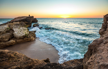 Fisherman on a high cliff over dramatic ocean at sunset