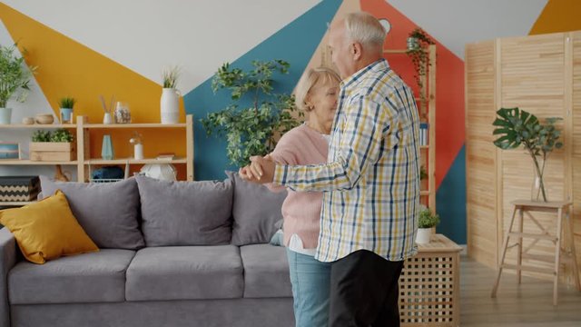 Slow motion of senior man and woman happy family dancing at home holding hands enjoying music together. Relationship, people and lifestyle concept.