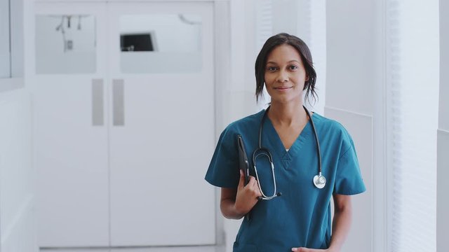 Portrait Of Female Doctor With Stethoscope Wearing Scrubs In Hospital Corridor With Digital Tablet