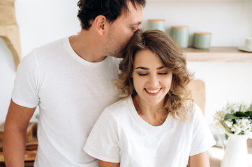 Close up portrait of an attractive couple in love in white t-shirts gently hugging in the kitchen