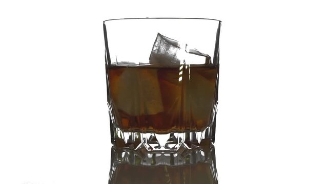 Ice cube falls and melts in a glass of whiskey. Rotating ice bubes in  whiskey on a white background.