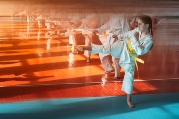 A teenage girl with a yellow belt in a karate class trains a direct kick. Beautiful morning light. Oriental martial arts. Children's training. No faces. With place for text. © Uladzimir