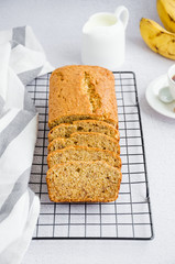 Homemade delicious banana bread with nuts and cinnamon on cooling rack with a cup of coffee, milk and fresh bananas Vertical orientation. Close up.