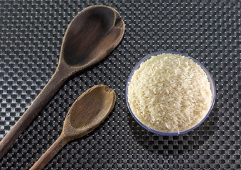 Grains of cereal rice on a dark background in a jar next to wooden spoon