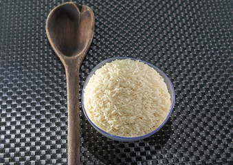 Grains of cereal rice on a dark background in a jar next to wooden spoon