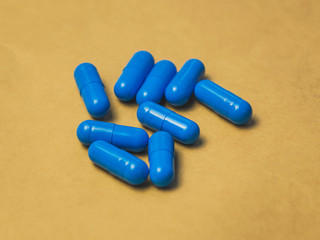 heap of blue capsule tablets on a brown background.