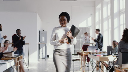 Happy smiling young African female manager entering new office with a box, welcomed by colleagues slow motion RED EPIC.