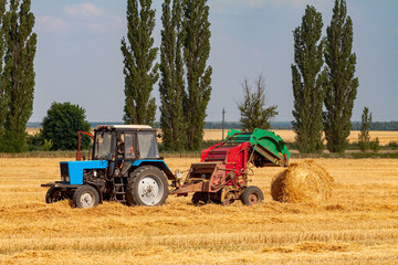 tractor makes big straw roll on yellow field at summer day