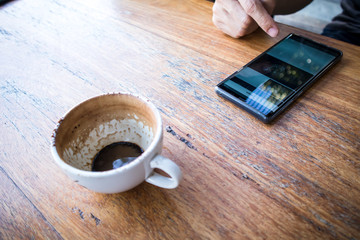 Close up of a right hand using smartphone with a Finished Empty Cup of Coffee