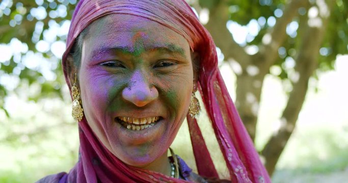Closeup face of a coloured Indian woman's face, wearing traditional jewelry and dress with pink scraf to covered head for respect outdoors,  during the festival of colour- Holi, celebrated in India