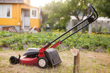 Fototapeta na wymiar Grass mower stands on green lawn in summer garden