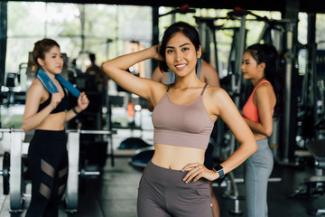 Fototapeta na wymiar Joyful young healthy Asian female trainer looking at camera while standing with multiracial friends in gym
