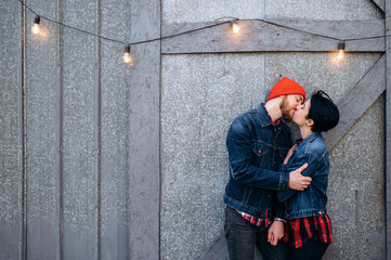 Attractive couple in casual wear is kissing against the gray background, outdoors