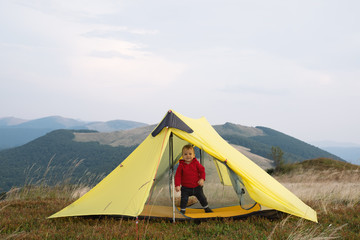 Small kid in yellow tent in spring mountains. Travel with child concept © Ivan Kmit