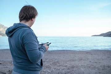 Man holding appliance for flying drone and mobile phone, making photo or video. Outdoors, beautiful sea view background, usage of modern wireless technology.