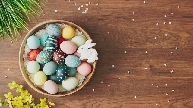 Hands putting down nest full of colorful Easter eggs on decorated wooden table. Easter holiday decorations, Easter concept background.