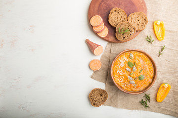 Sweet potato or batata cream soup with sesame seeds in a wooden bowl on a white wooden background. top view, copy space.