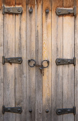Vintage wooden window shutters with rusty iron hinges and padlock on chain in Nesebar. Closed rustic raw wooden shutters