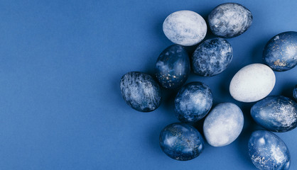 Beautiful group ombre blue Easter eggs with quail eggs and feathers on a blue background. Easter concept. Border eggs. Copy space for text