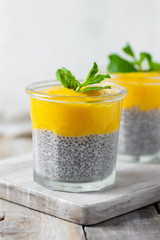Healthy and delicious homemade vegan breakfast, simple and light meal - chia pudding prepared with coconut or rice milk with ripe mango puree on top. Fresh green mint. Wooden backgroun