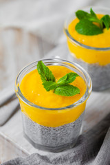 Healthy and delicious homemade vegan breakfast, simple and light meal - chia pudding prepared with coconut or rice milk with ripe mango puree on top. Fresh green mint. Wooden backgroun