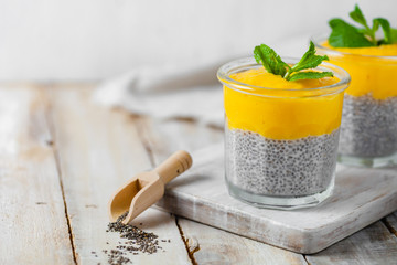 Healthy and delicious homemade vegan breakfast, simple and light meal - chia pudding prepared with coconut or rice milk with ripe mango puree on top. Fresh green mint. Wooden background, copy space