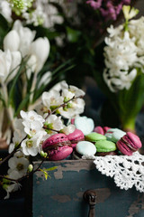 Obraz na płótnie Canvas Beautiful Easter composition with bright delicious homemade traditional french dessert - elegant macarons. Floral decor, spring flowers on background, vintage wooden box. Front view, close up.