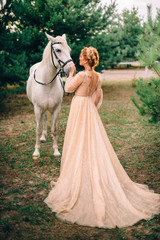 Fototapeta premium Young woman in a gold dress leans her head against a white horse, Full-length portrait.