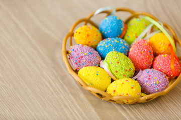Colorful easter eggs in basket and mimosa flowers on wooden table. Top view with copy space
