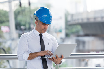 Engineering man wear blue helmet working with laptop outdoor building office.