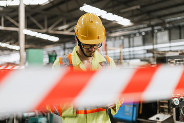 Industrial man wearing uniform safety and helmet in factory blurred foreground, space barrier tape...