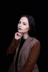 Cute girl dressed in casual wear is smiling with a hand under the chin on black background 