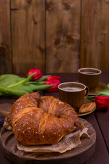 Easter breakfast with aromatic fresh espresso, croissants, colored eggs, red tulips and willow. Coffee with pastries, flowers on a wooden table. View from above. Copy space.