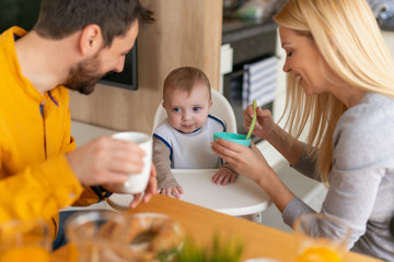 Father and mother feeding their son in the kitchen at home