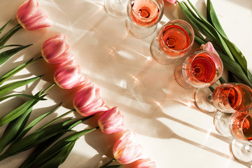 Pink tulips lie in row opposite row of glasses with red wine or champagne on white table. Free...