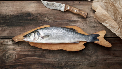 fresh whole sea bass fish on brown cutting board