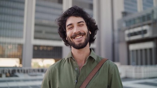 Portrait of a smiling young professional man standing in front of corporate building looking at camera
