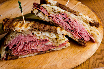 Reuben Sandwich, classic traditional American bar/pub menu item, on grilled rye bread, corned beef, Swiss cheese, sauerkraut and topped with thousand island dressing and french fries in background.
