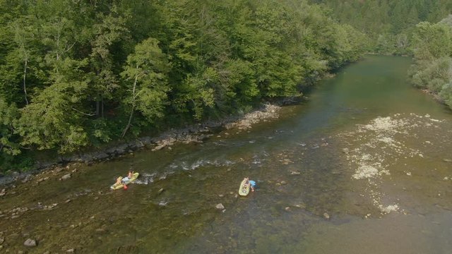 AERIAL: Group of young tourists on push their rafts into the calm Kolpa river. Travelers on an active vacation in Slovenia paddle their rubber boats down a tranquil river. Fun summer outdoor activity.