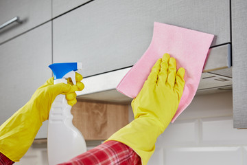 Close up hands in protective yellow gloves cleaning the kitchen metal extractor hood with rag and spray bottle detergen