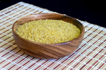 Dry bulgur close-up in a wooden bowl on a bamboo stand. Concept of Oriental cuisine dishes