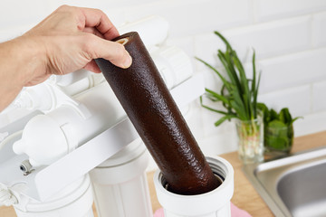 Plumber or man hand holding dirty cartridge for replace at home kitchen. Fix purification osmosis...