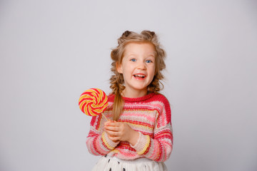 portrait of a girl a blonde child with a Lollipop on a stick smiling in colored clothes on a white background