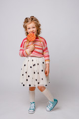portrait of a girl a blonde child with a Lollipop on a stick smiling in colored clothes on a white background
