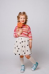 portrait of a girl a blonde child with a Lollipop on a stick smiling in colored clothes on a white background